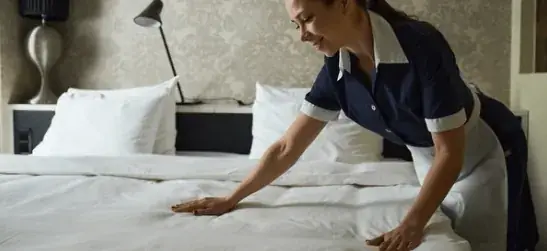 Housekeeper arrumando a cama em um quarto de hotel
